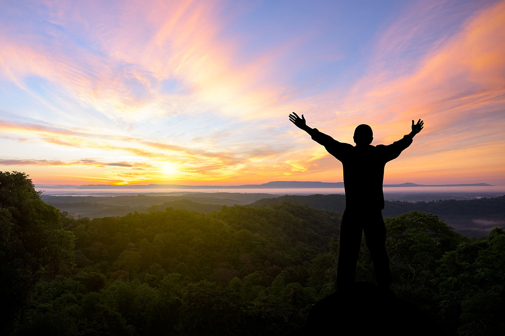 Person raising hands over head in front of sunset