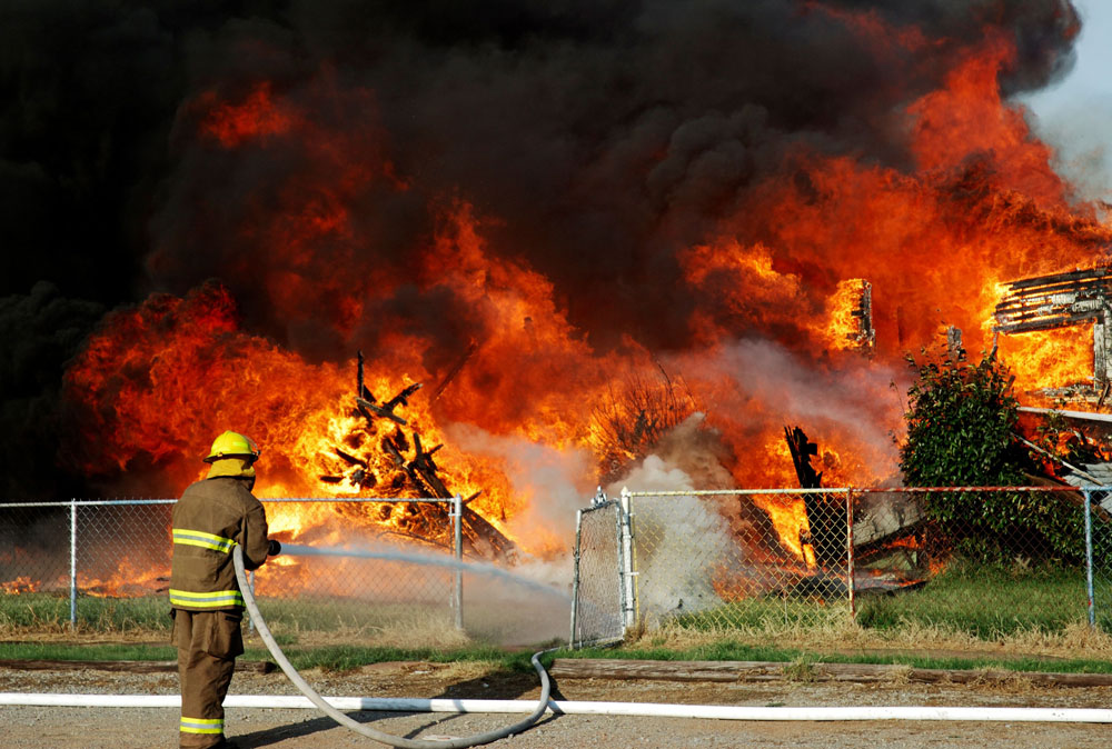 Firefighter spraying water on a burning house
