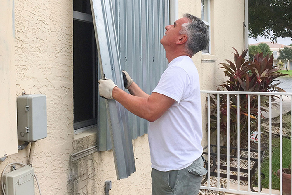 Man installing hurricane shutters before a storm