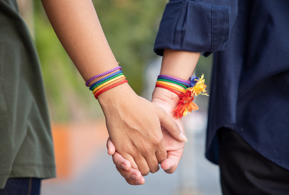 Two people holding hands with rainbow bracelets on 