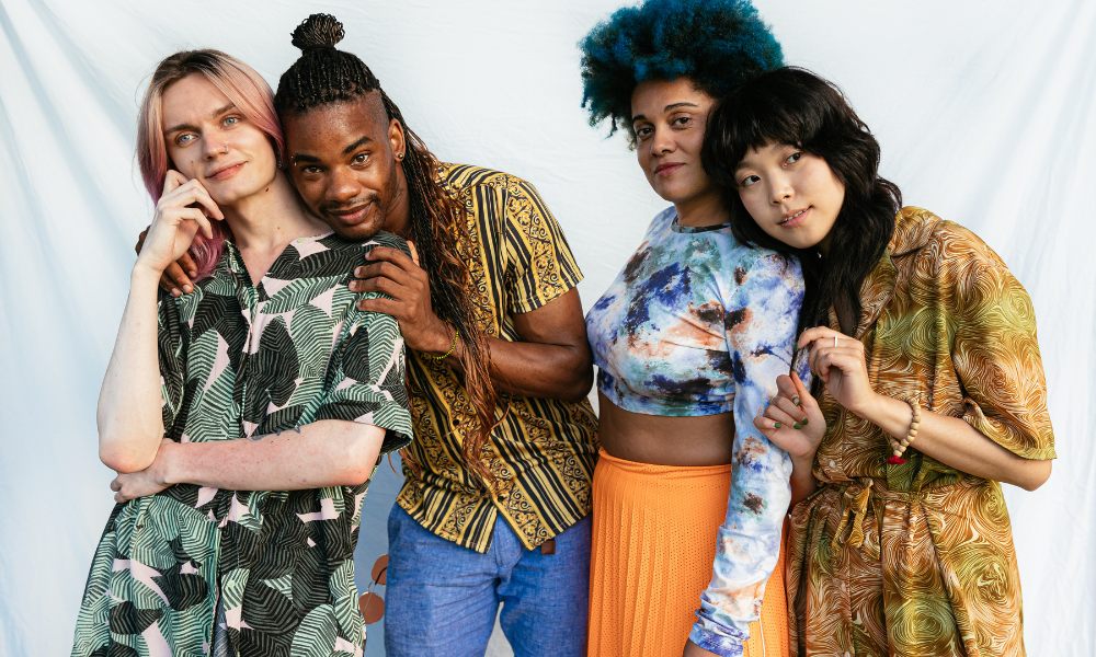 A diverse group of four people standing close together, smiling and showing connection and support. The image represents inclusion, resilience, and community-based healing.