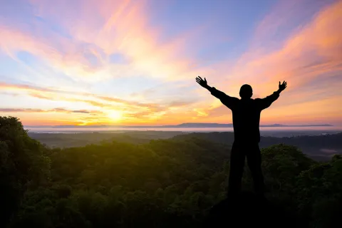 Person raising their hands in the air in triumph with sunset in background