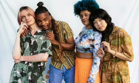 A diverse group of four people standing close together, smiling and showing connection and support. The image represents inclusion, resilience, and community-based healing.
