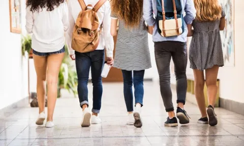 Five teenagers walking down a bright school hallway with backpacks, representing connection, support, and resilience through the GRIT-TEEN program.