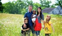 Family standing in a field of grass next to a barn